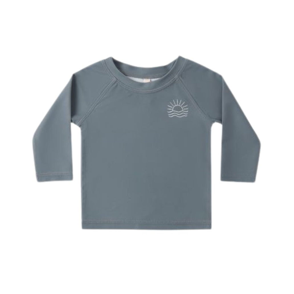 A toddler's long-sleeve rash guard in a muted slate blue-gray color, featuring a small white sun and wave graphic on the left chest, displayed against a solid white background.