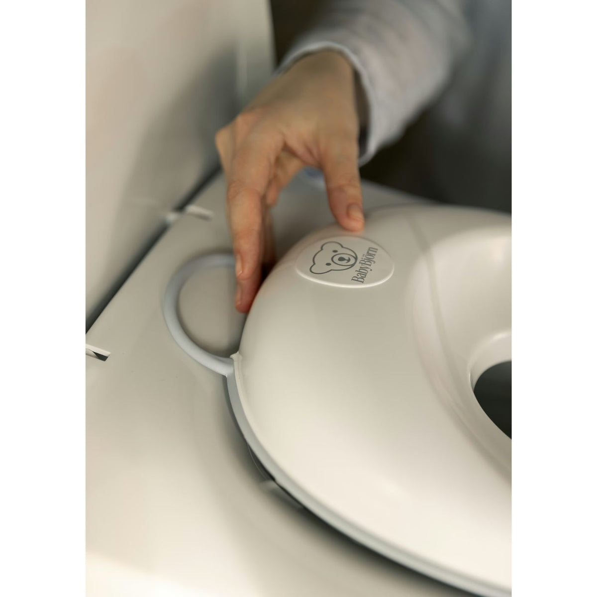 Hand pressing a button on a white appliance with a brand logo.