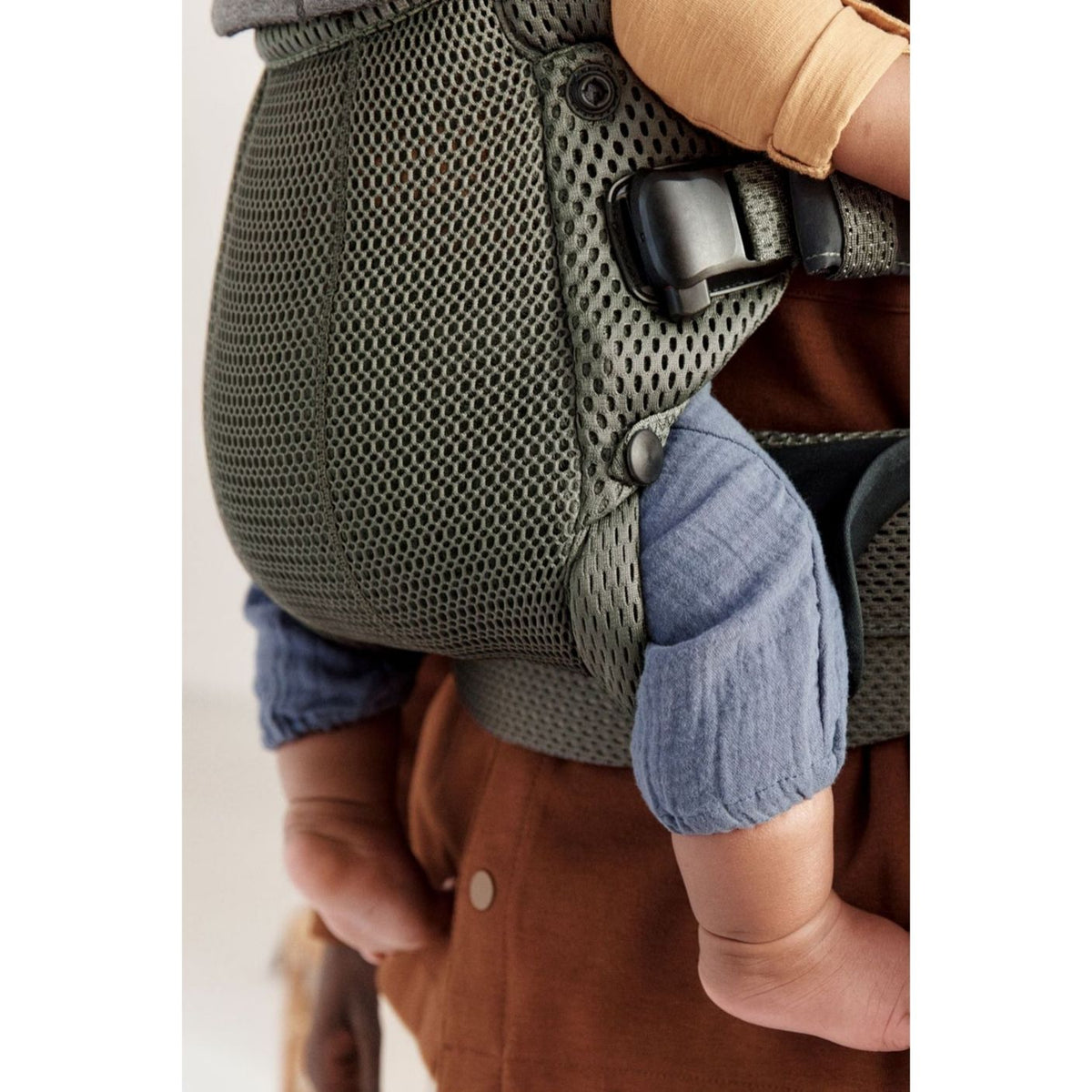 Close-up of a baby in a green carrier with a blurred background
