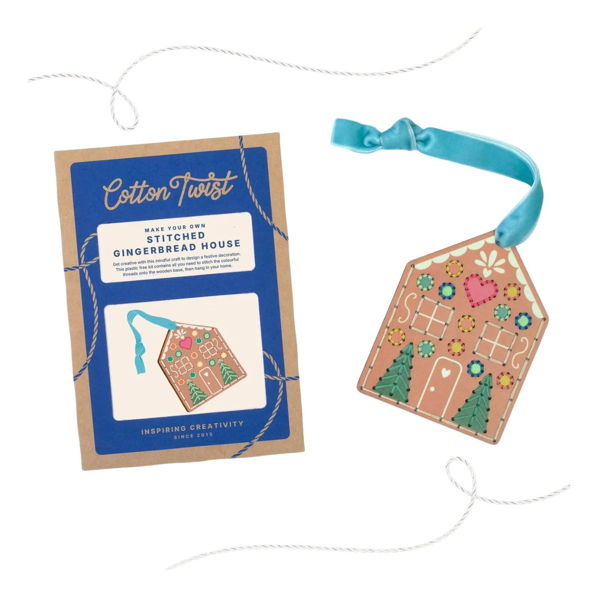 A craft kit package labeled 'Cotton Twist' next to a finished gingerbread house ornament. The package has a blue label on kraft paper and shows a stitched gingerbread house illustration with a blue ribbon.