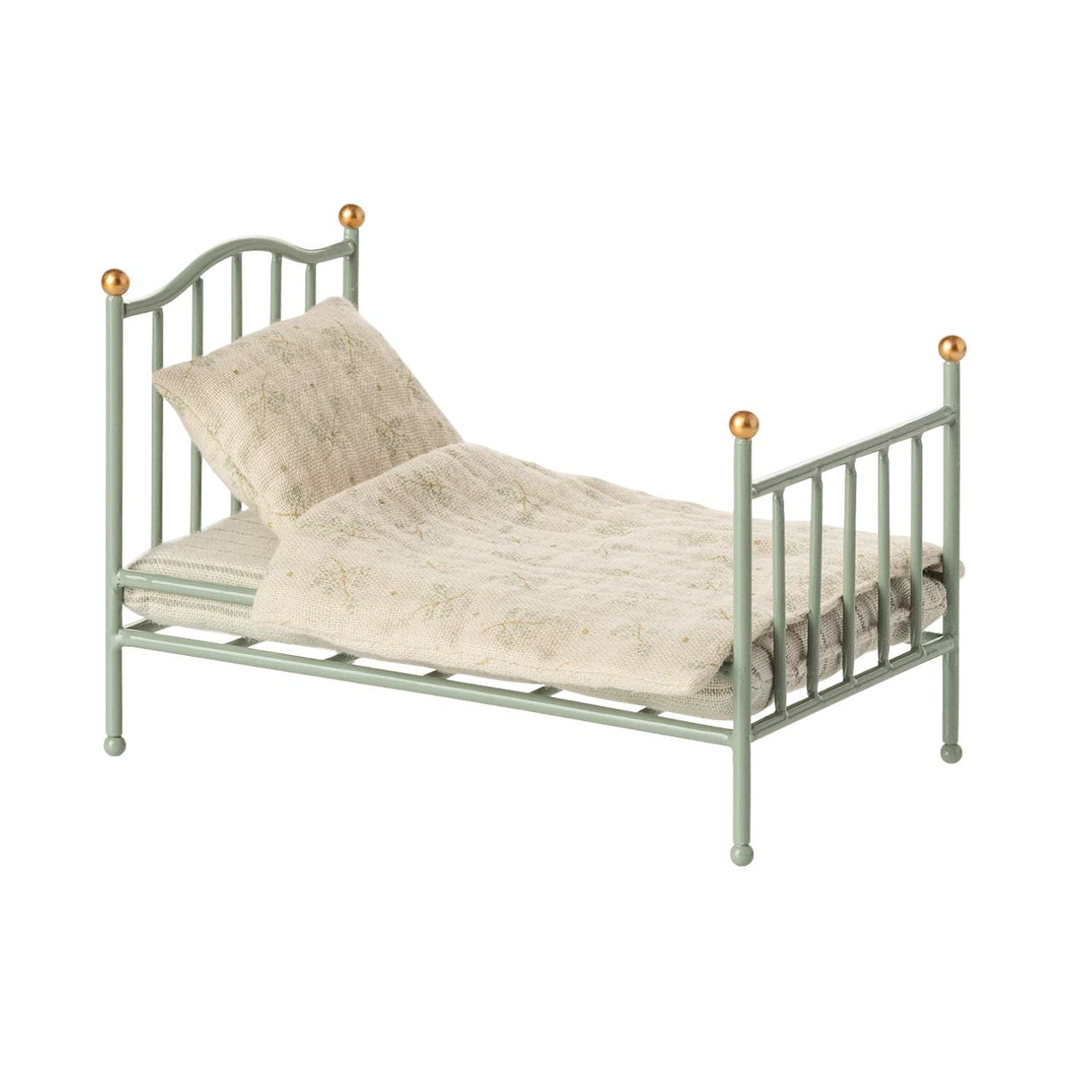 A mint green miniature metal single bed by Maileg, featuring vintage-inspired vertical bars, gold-colored spherical knobs on the posts, and a cozy patterned mattress, pillow, and blanket set against a plain white background.