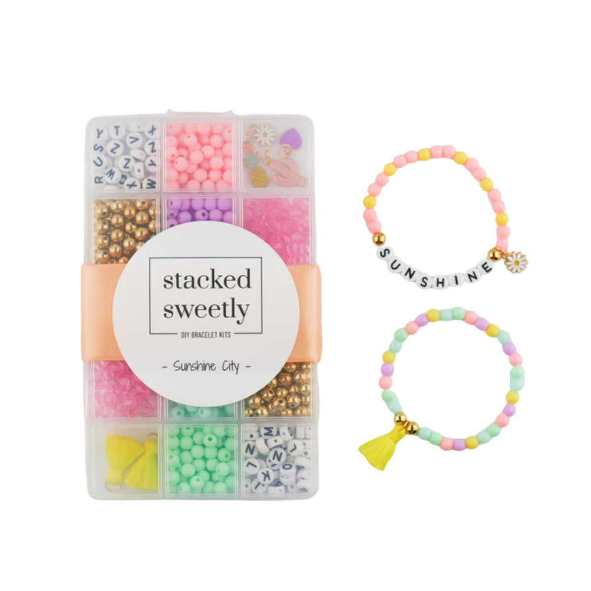 A DIY bracelet kit in a clear compartmentalized storage box filled with colorful beads, alphabet beads, and charms, displayed next to two completed stretchy pastel bead bracelets spelling out "SUNSHINE" alongside a tassel and flower charm.