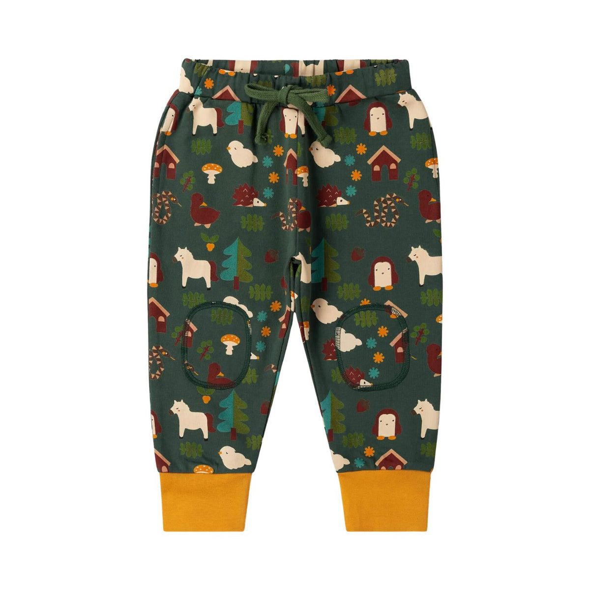 A pair of children's jogger pants with a forest-themed print on a dark green background, featuring woodland motifs like trees, mushrooms, houses, and animals. The pants have a matching green drawstring waist and solid mustard yellow cuffs.
