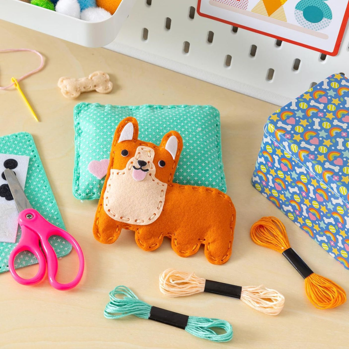 Felt craft project with a dog design, scissors, thread, and patterned paper on a wooden surface.