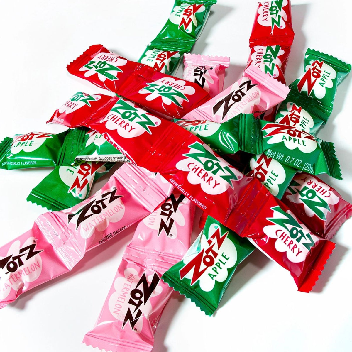 A pile of Zots Apple candy wrappers in red, green, and pink, arranged on a clean white background.