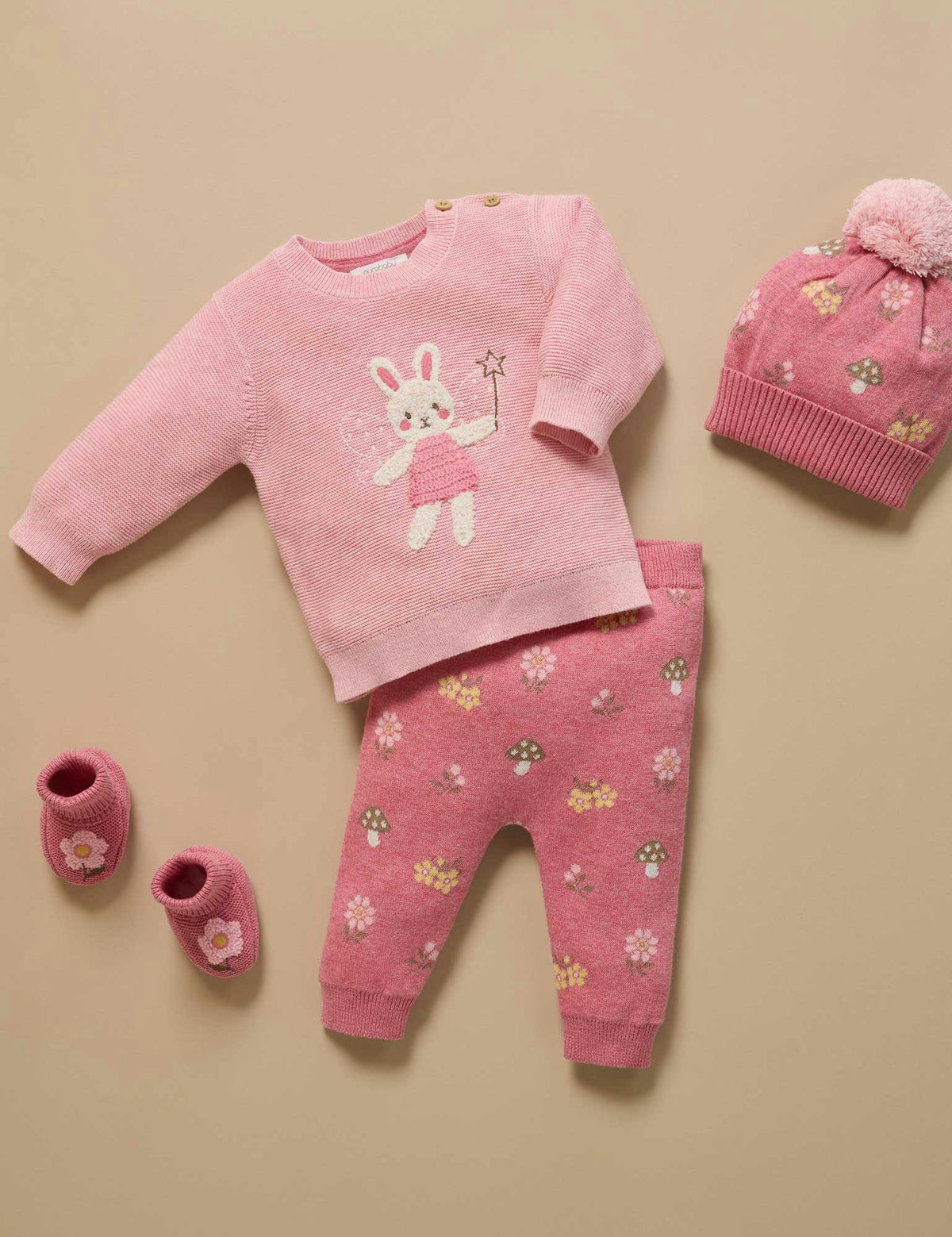 Pink baby outfit with sweater, pants, hat, and shoes on a beige background