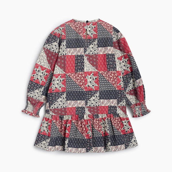 The Quill Dress by The New Society shown laid flat against a white background, featuring a vintage-inspired patch-style print in deep red and blue tones, long sleeves, and a ruffled hem.