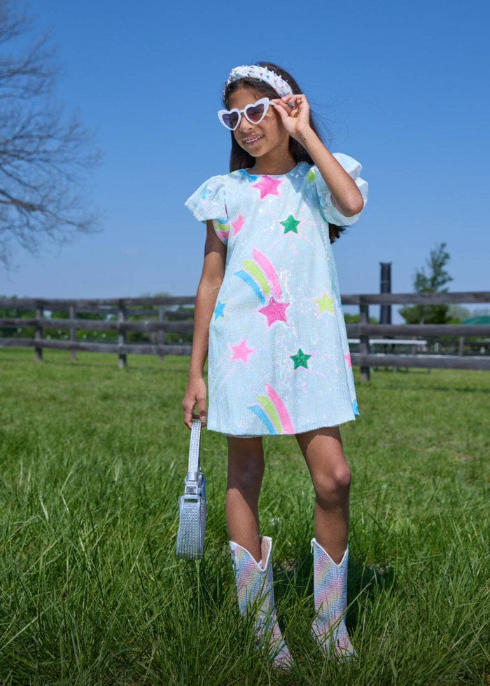 Young girl in a light blue dress with colorful patterns standing in a grassy field.