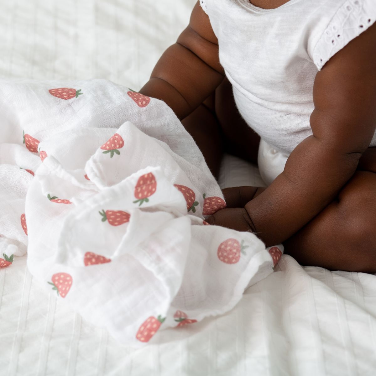Person sitting on a bed with strawberry-patterned white blanket