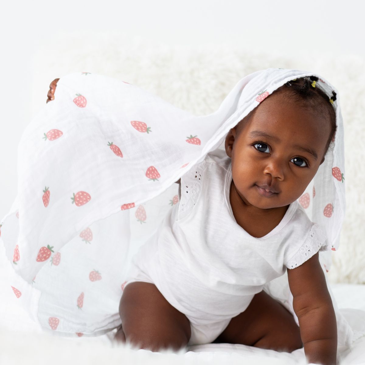 Baby wearing a white outfit with strawberry patterned cover-up on a white background