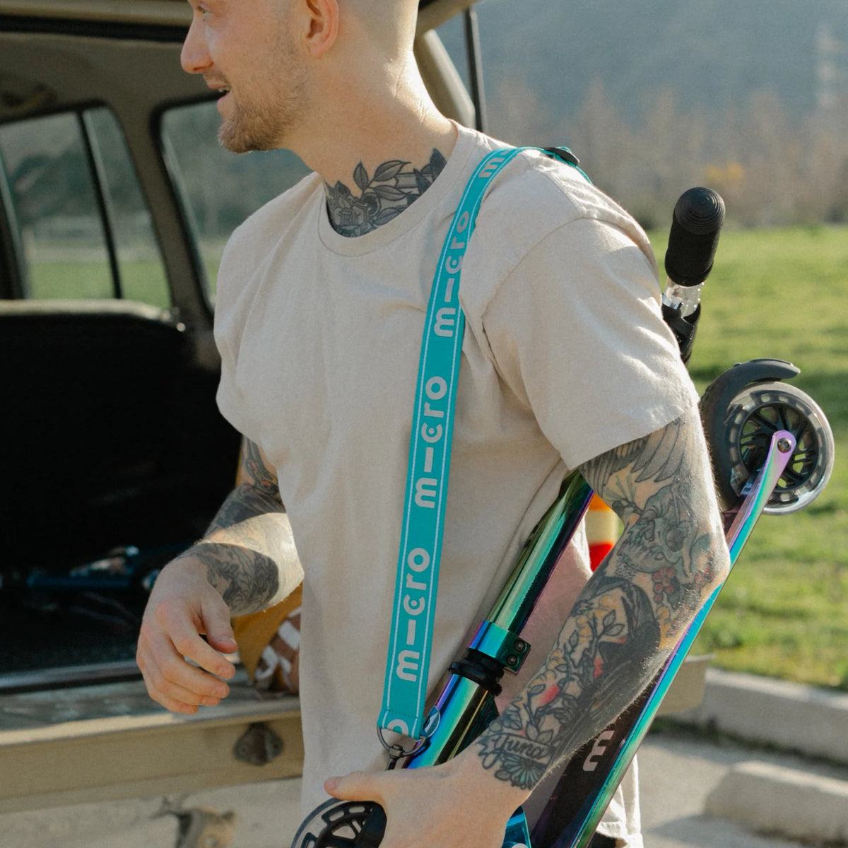 Man holding a skateboard with a tattooed arm, standing next to an open car trunk.