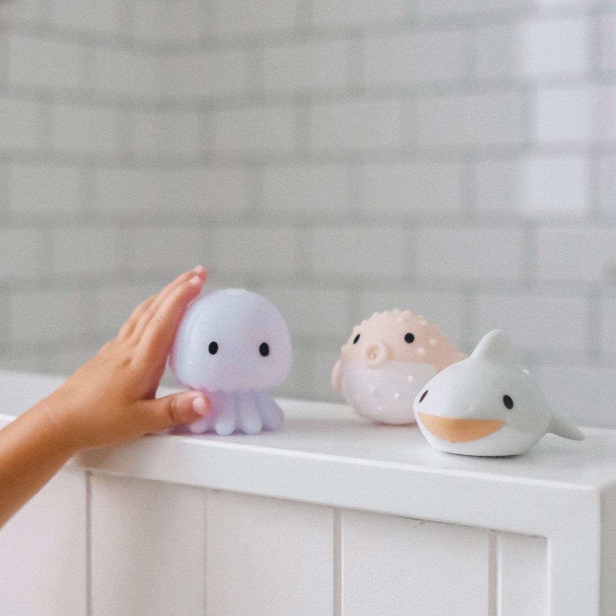 Person holding a small octopus-shaped light next to two other animal-shaped lights on a white surface.