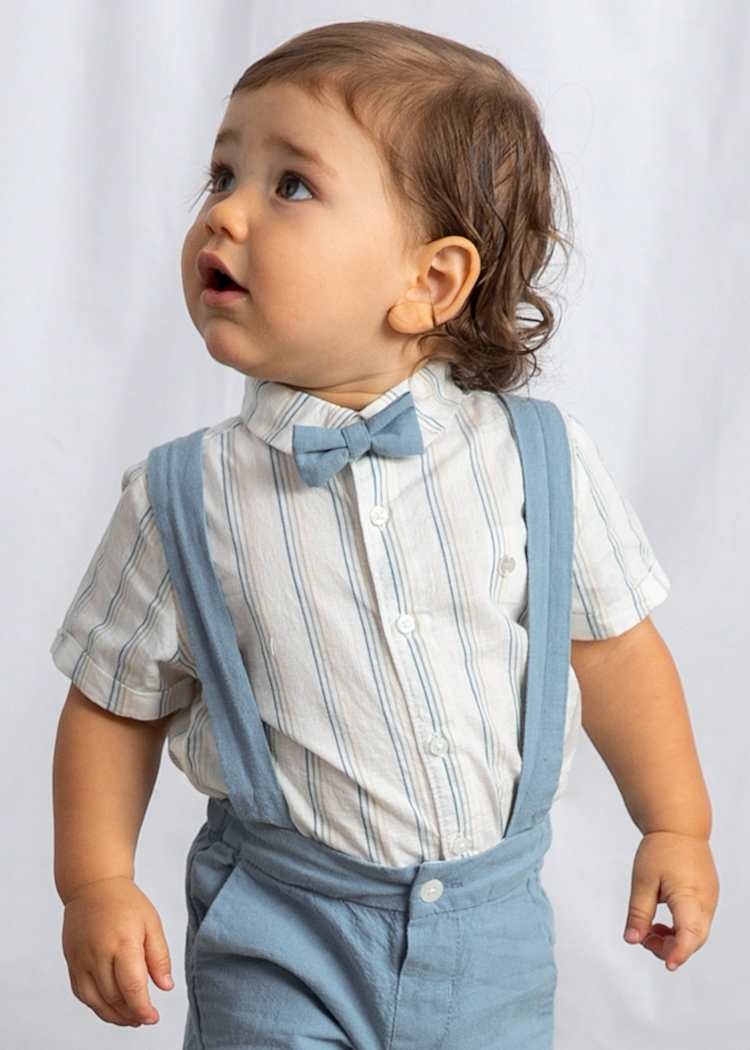 Child wearing a striped shirt, bow tie, and blue suspenders against a plain background