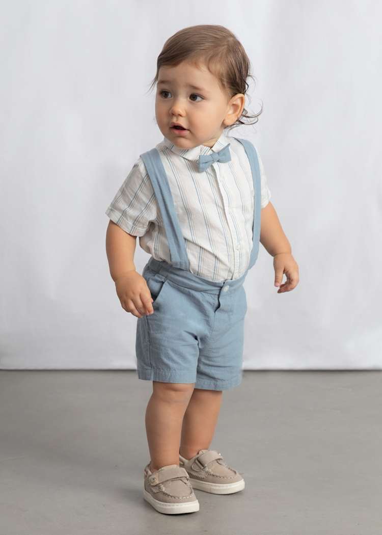 Child wearing a light blue outfit with suspenders against a plain background