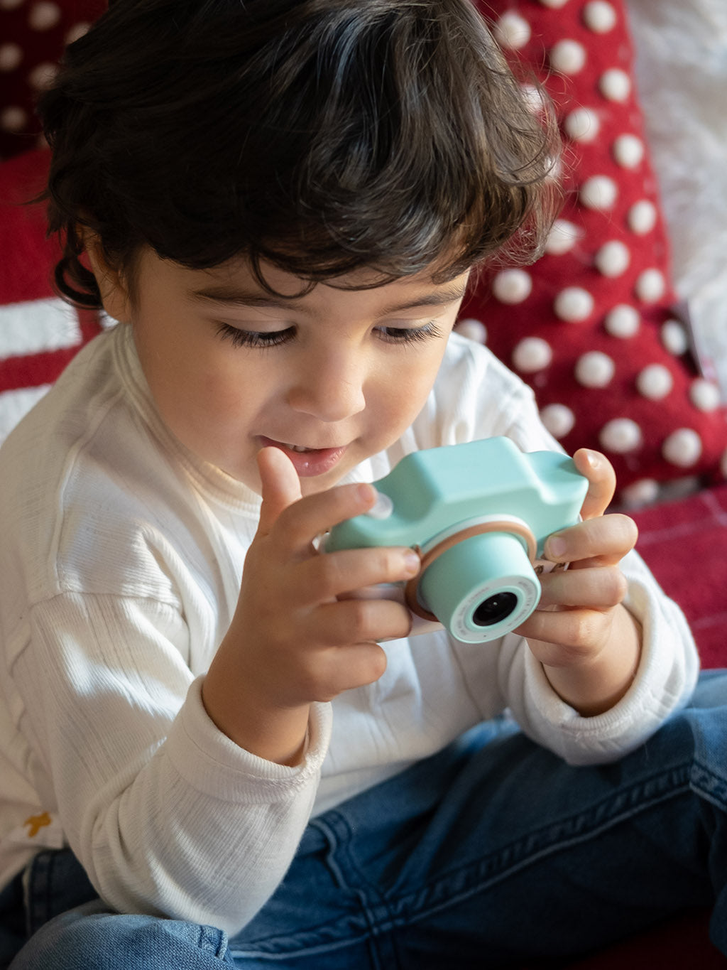 Child playing with a teal toy camera on a red and white polka dot blanket