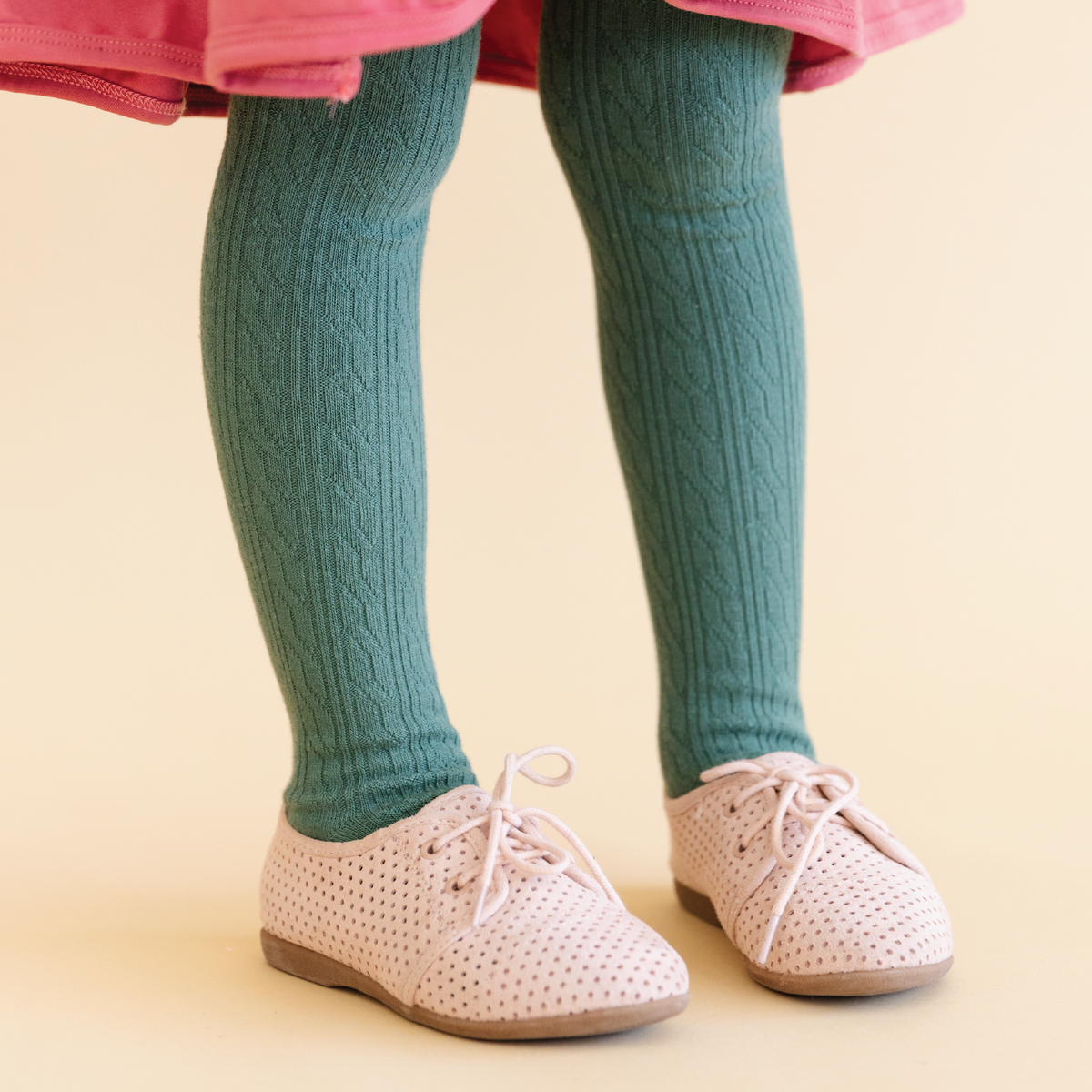 Children's legs wearing green tights and pink shoes on a beige background