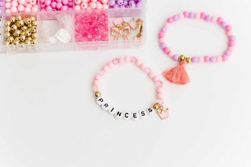 Princess Party DIY Bracelet Kit featuring an open compartment storage box filled with colorful beads, alphabet letter beads, and charms next to two completed beaded bracelets, including one with a tassel charm and one spelling "PRINCESS".