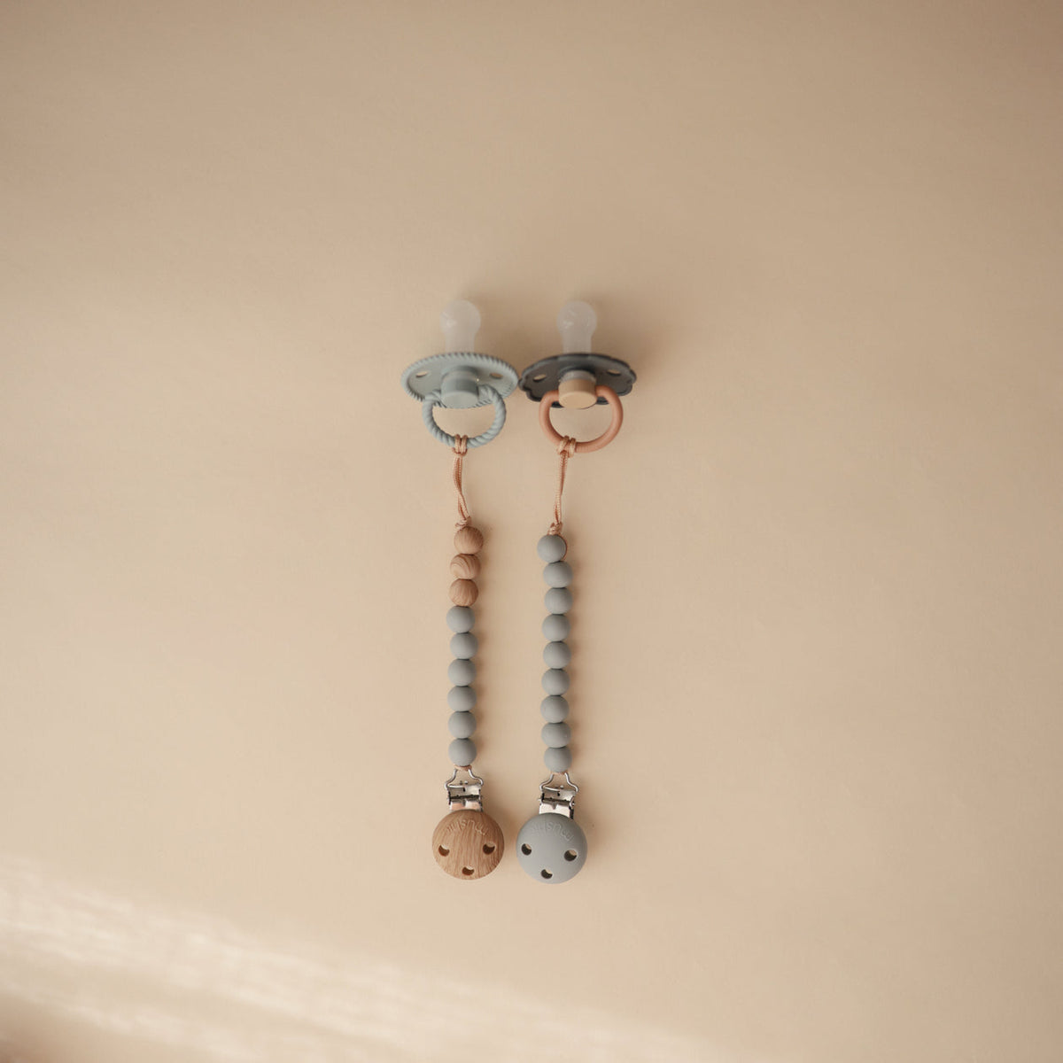 Two baby pacifiers with beaded chains on a beige background