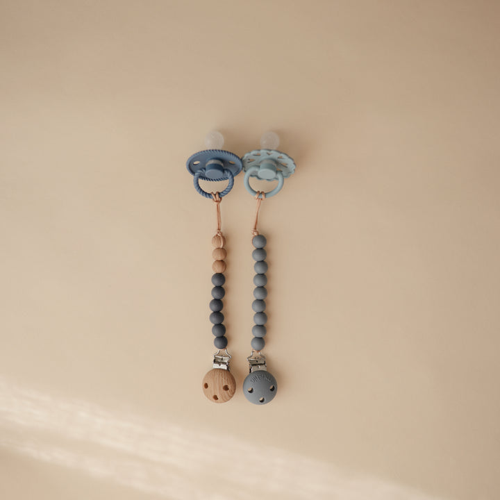 Two baby pacifiers with beaded chains on a beige background