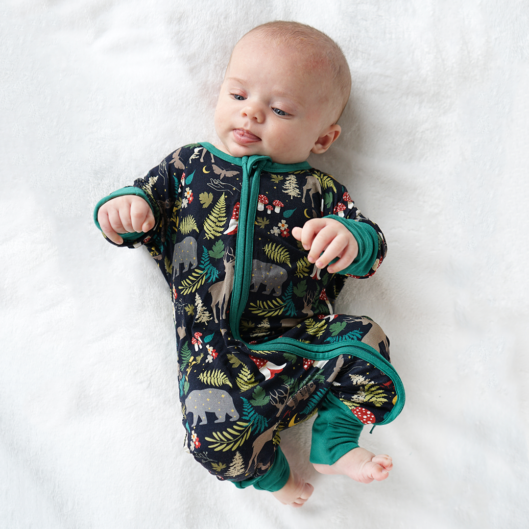 Baby wearing a forest-themed onesie on a white blanket