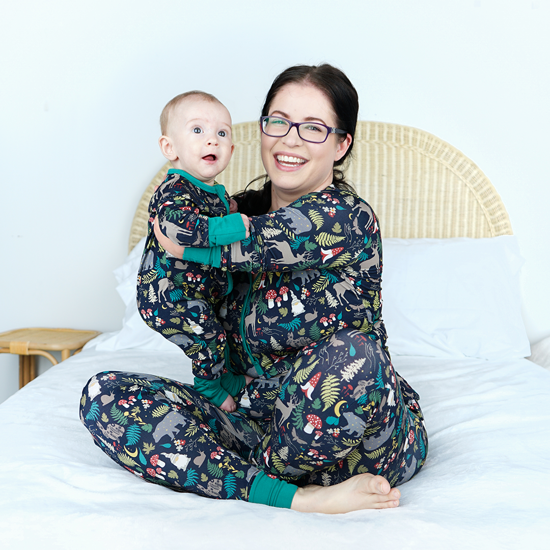 Woman and child wearing matching pajamas with a forest design on a bed.