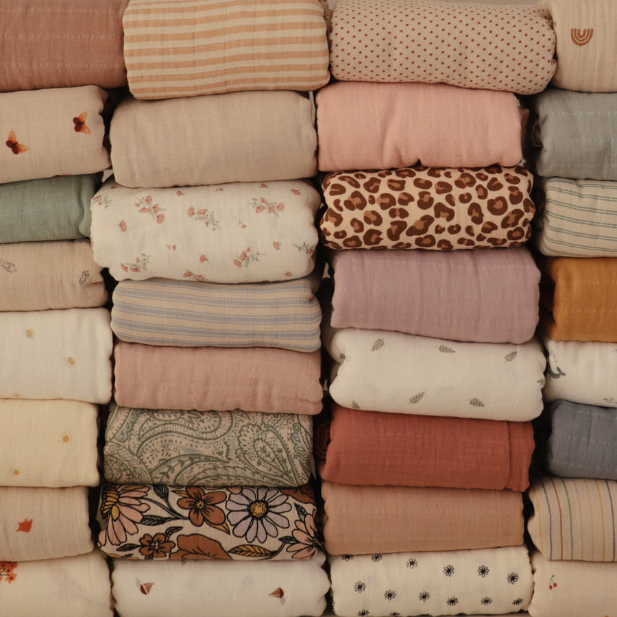 A neatly stacked arrangement of various patterned baby swaddle blankets and crib sheets.