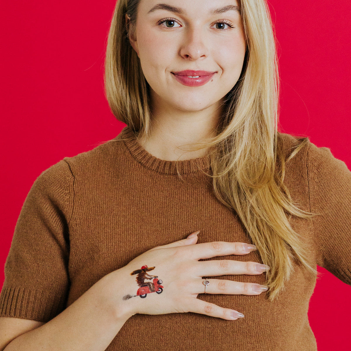 Woman wearing a temporary tattoo of a dog on a scooter against a red background