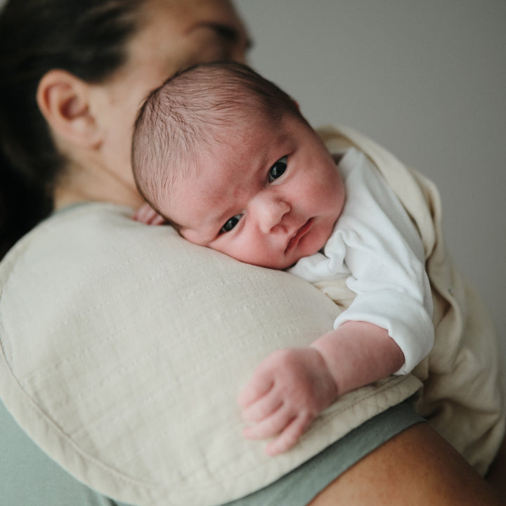 Newborn baby being held by a person wearing a beige wrap.