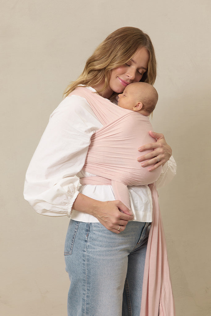 Woman holding a baby in a pink wrap against a beige background