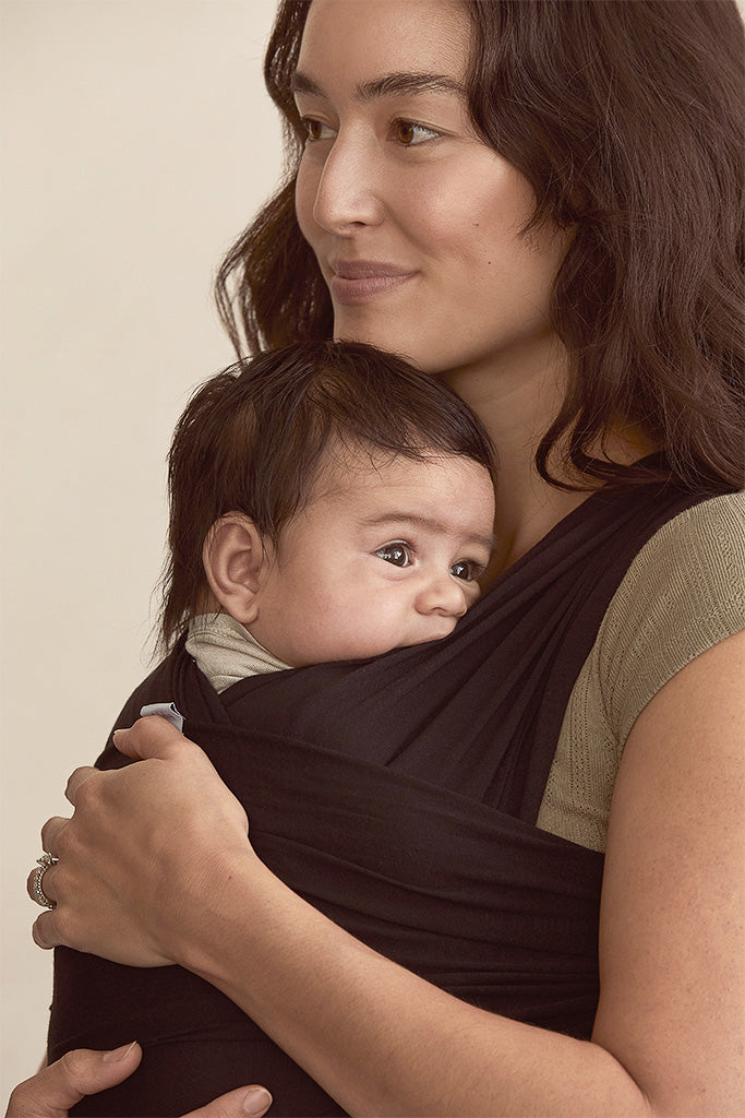 Woman holding a baby in a sling against a plain background