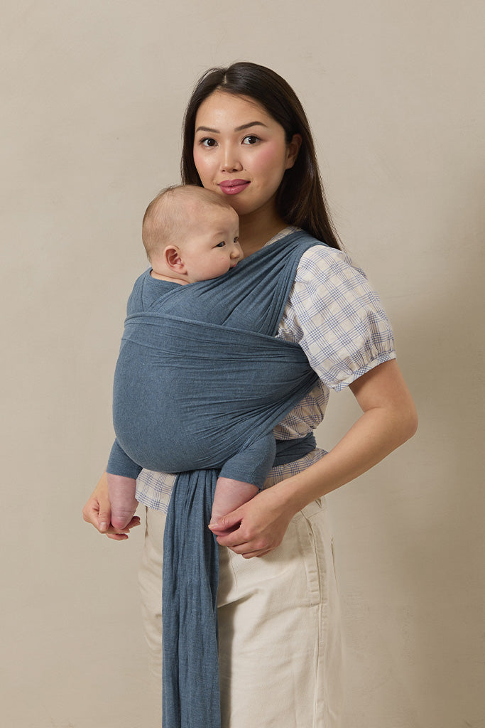 Woman holding a baby in a blue sling against a beige background