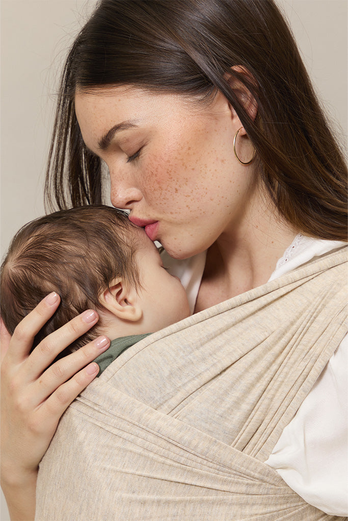 Woman holding a baby in a beige wrap against a neutral background