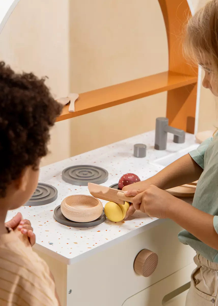 Two children playing with a wooden toy kitchen set.