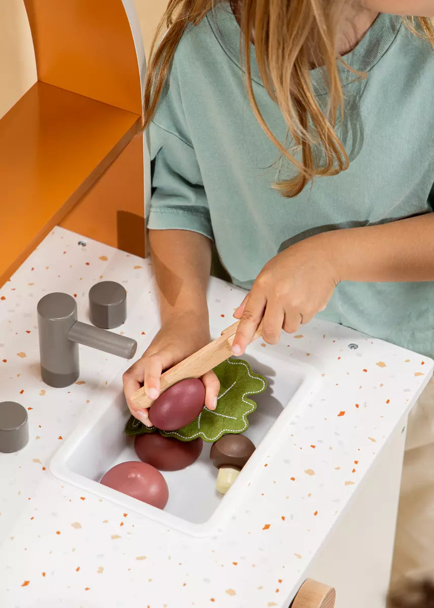 Child playing with toy fruits and a wooden knife on a white tray with orange speckles.
