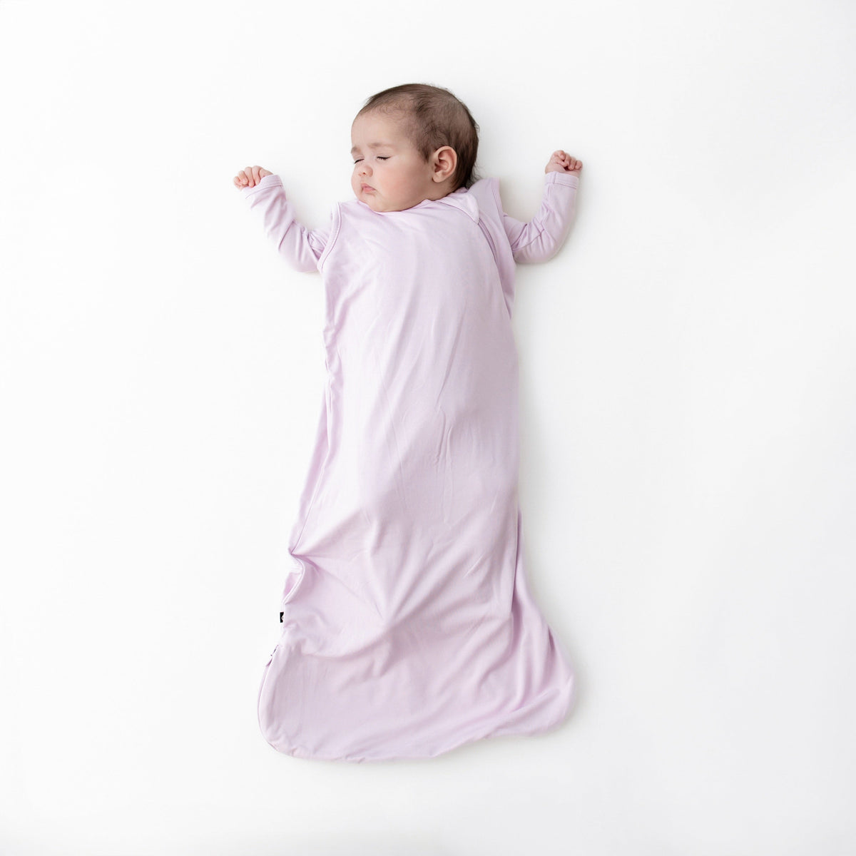 Baby in a pink sleep bag lying on a white background