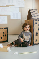 Child playing with a cardboard house on a light-colored floor.