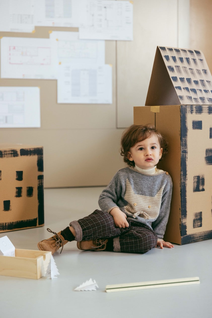Child playing with a cardboard house on a light-colored floor.