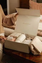 Person opening a white box containing a skincare product on a wooden table.