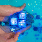 Hand holding blue LED dice with robot faces against a blue glittery background