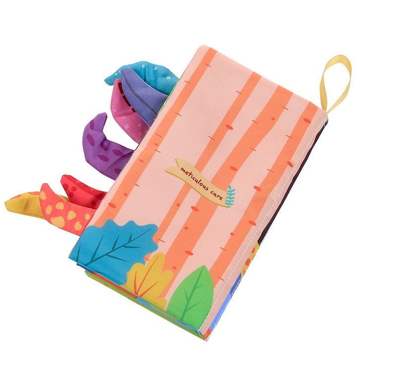 A baby sensory toy book with a soft cover featuring orange and pink vertical stripes, a small yellow label reading 'sensory care', colorful fabric dinosaur tails, and a yellow loop handle, shown on a white background.