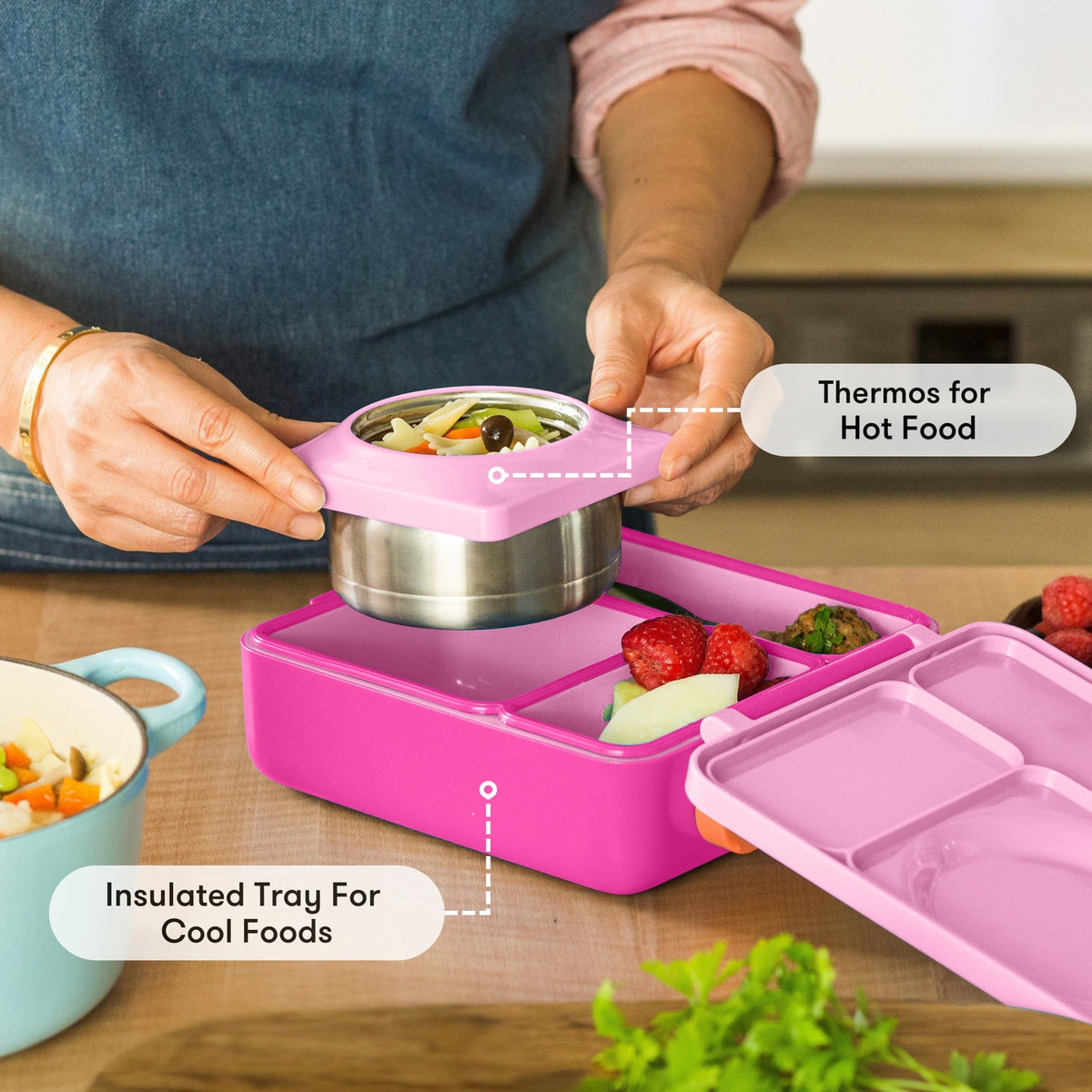 Pink lunch box with compartments and a thermos for hot food, on a wooden table.