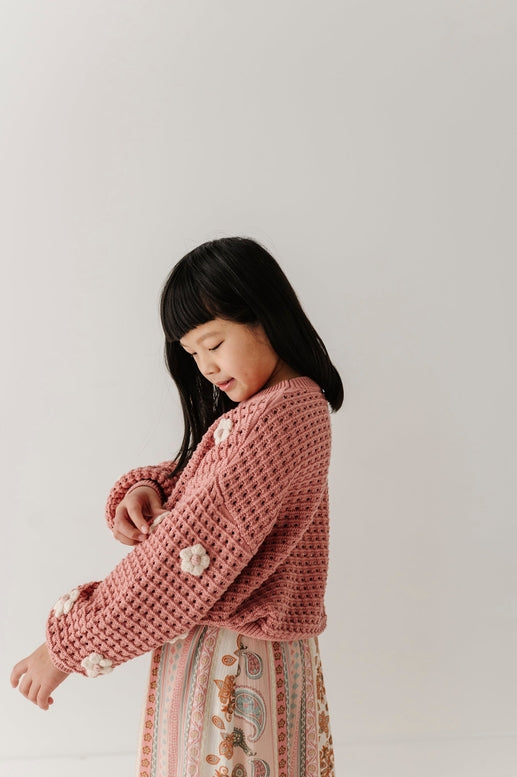 Young girl wearing a pink knitted sweater with white flowers on a plain background