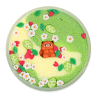 A round decorative dish or tray filled with pastel glittery slime or wax art, featuring a small orange racoon figure in the center, surrounded by green, leaves, flowers, and hearts embellishments on a black background.