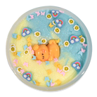 A round decorative dish or tray filled with pastel glittery slime or wax art, featuring a small orange bear figure in the center, surrounded by rainbow, sunflower, butterfly, and star embellishments on a white background.