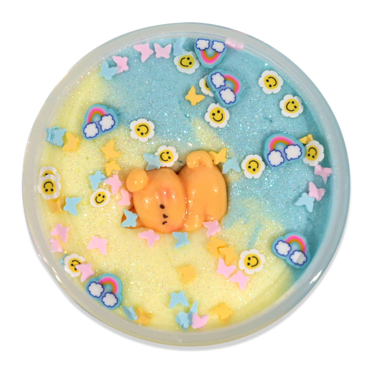 A round decorative dish or tray filled with pastel glittery slime or wax art, featuring a small orange bear figure in the center, surrounded by rainbow, sunflower, butterfly, and star embellishments on a white background.