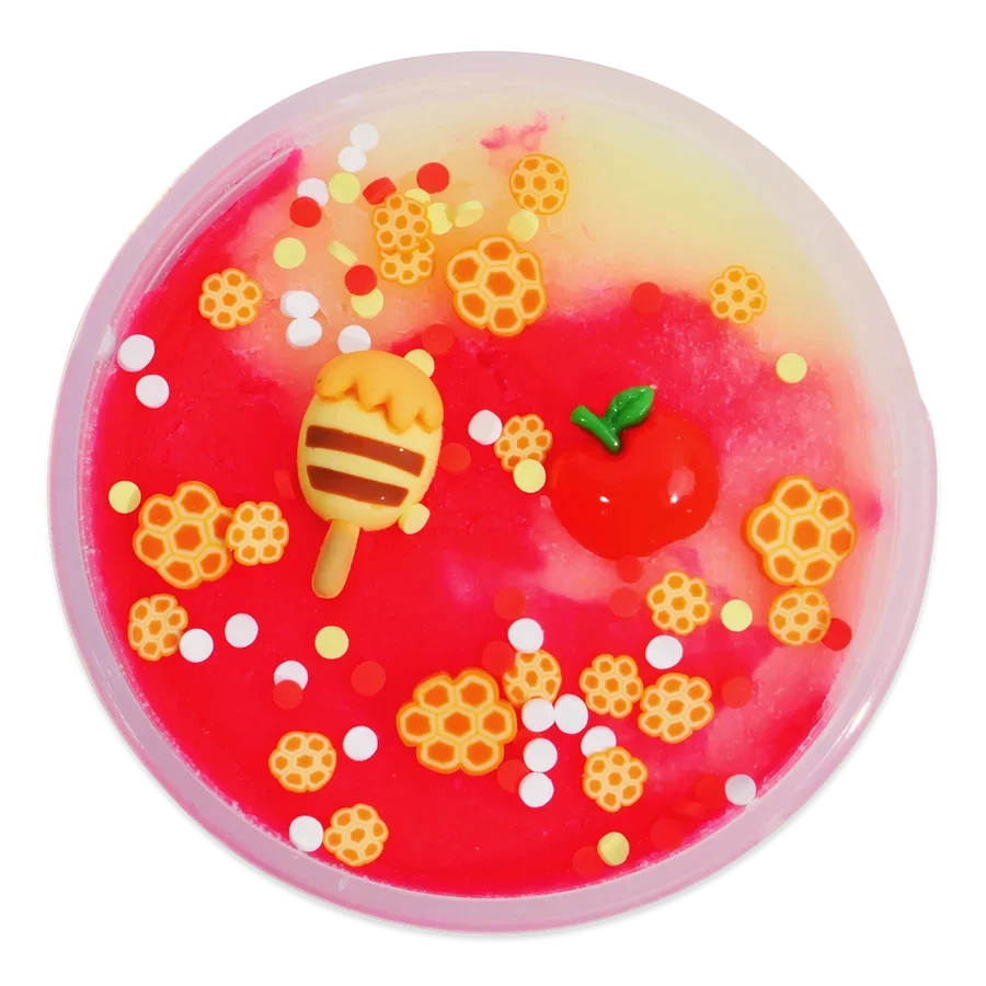 A round, translucent pink and yellow gel toy filled with colorful decorative elements, including honeycomb shapes, white dots, a small red apple with a green leaf, and a striped honey pot decoration, shown on a plain white background.