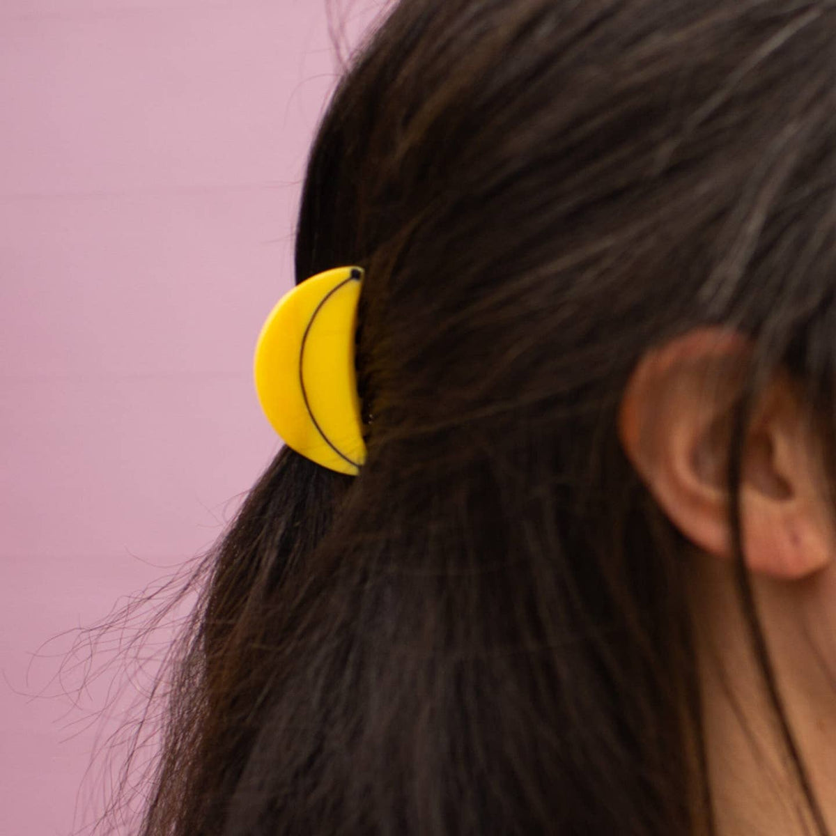 Yellow hair clip on dark hair against a pink background