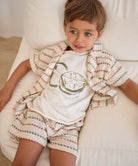 Child wearing a patterned shirt and shorts sitting on a white couch.
