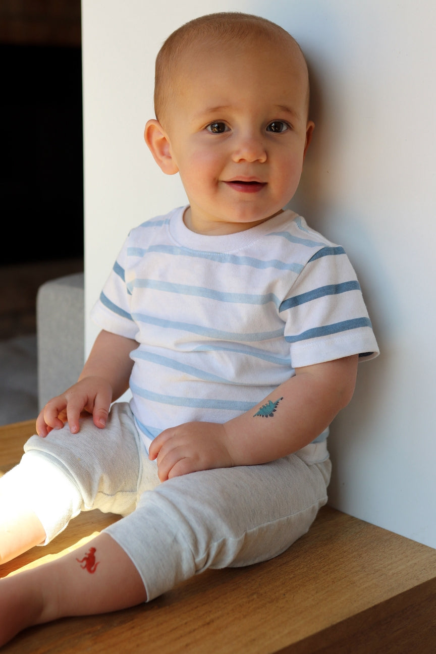 Baby wearing a striped shirt sitting on a wooden surface.
