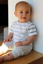 Baby wearing a striped shirt sitting on a wooden surface.